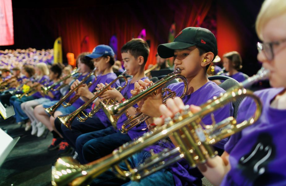 Unga musiker iklädda lila tröjor spelar blåsinstrument. Bilden är tagen från sidan.
