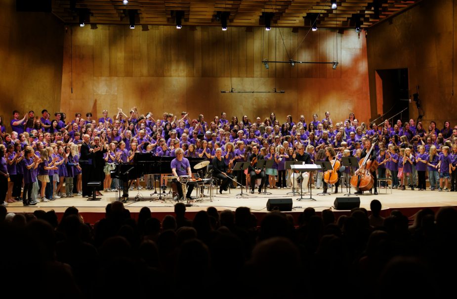 Unga musiker iklädda lila tröjor spelar tillsammans på scen.