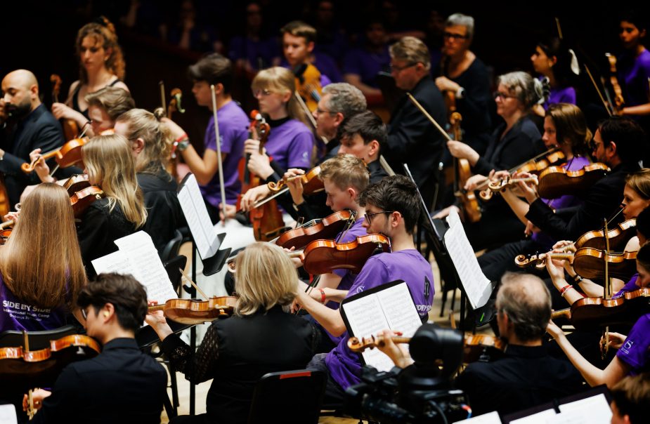 Unga musiker iklädda lila tröjor spelar tillsammans på scen.