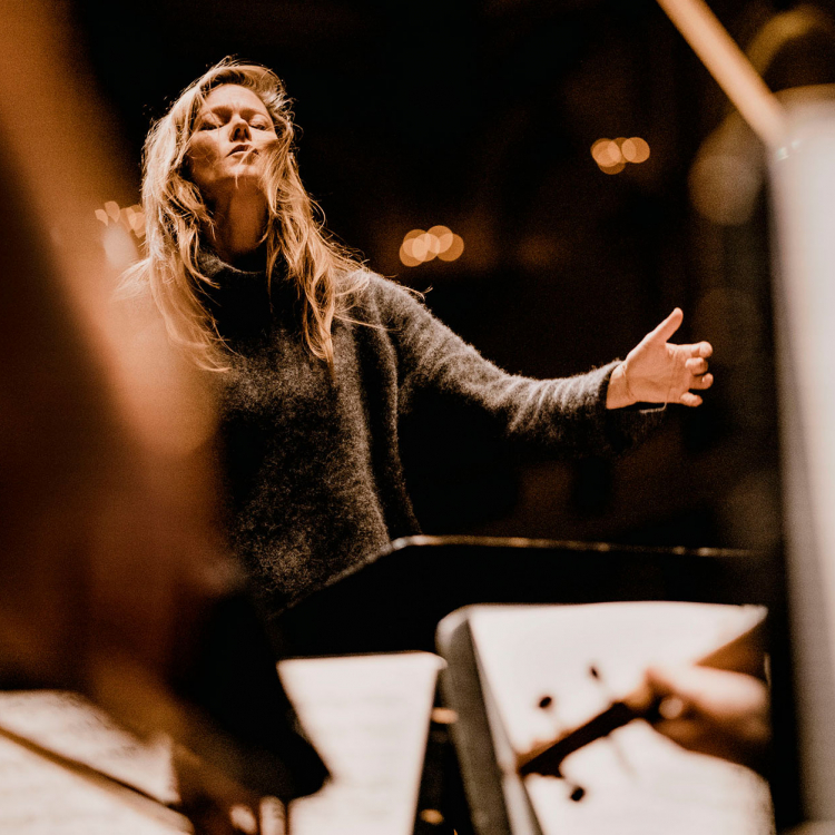 Dirigenten Barbara Hannigan i innerlig pose på pulten, med håret utslaget och händerna framför sig, riktade mot orkestermusikerna.