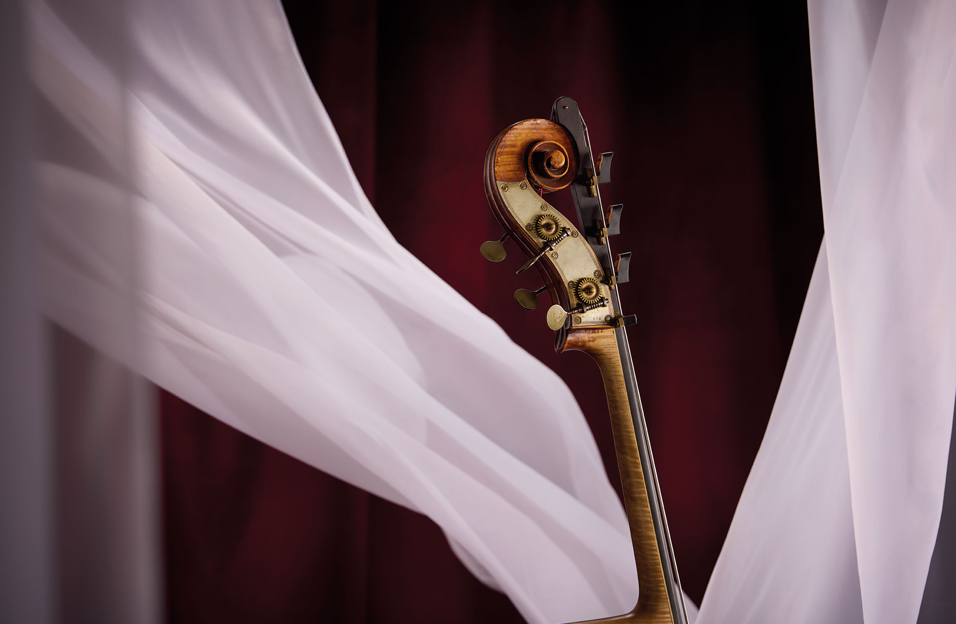 Översta delen på en kontrabas i miljö med vita tyger mot röd bakgrund.