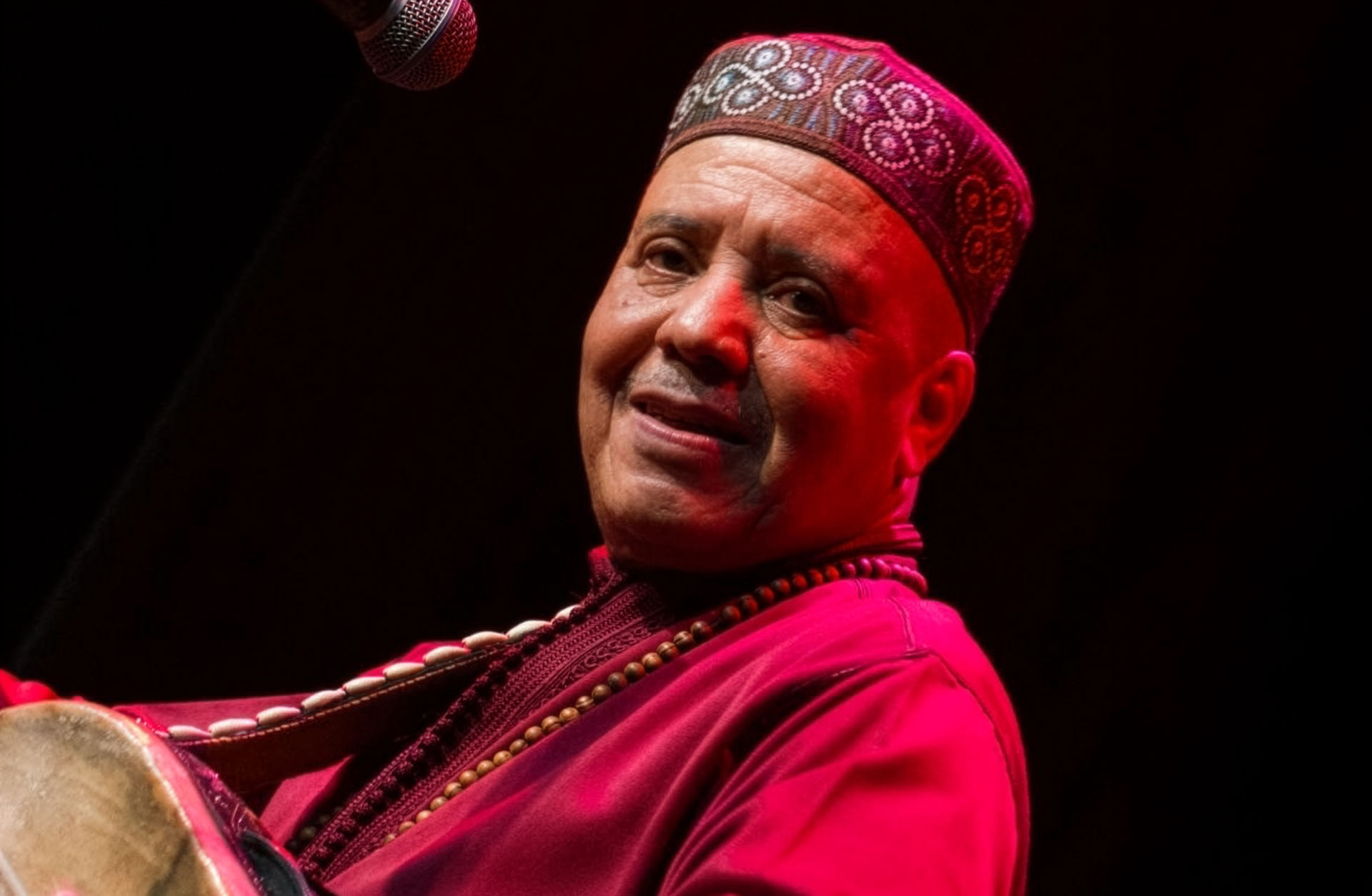 Man iklädd rösaröda kläder tittar in i kameran. Bilden är tagen i profil mot mörk bakgrund.