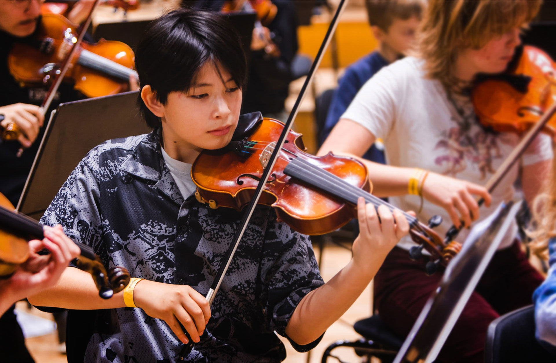 Ung violinist spelar på sitt instrument på scen, omgiven av andra unga musiker.