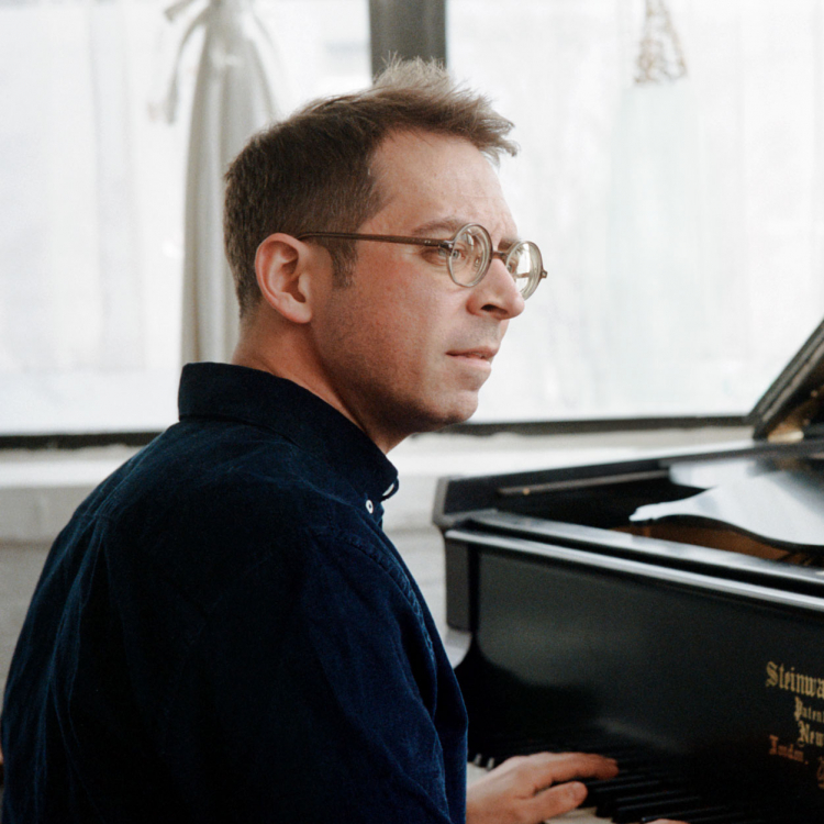 Pianist sitter med ryggen åt kameran och tittar åt sidan. Framför honom syns pianot.