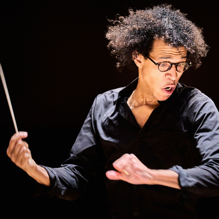 Dirigent in action mot mörk bakgrund. Intensiv bild där håret flyger i luften.