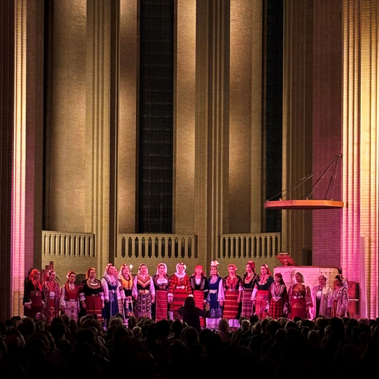 Kör på pampig scen. Rosa ljus lyser upp de många körmedlemmarna.