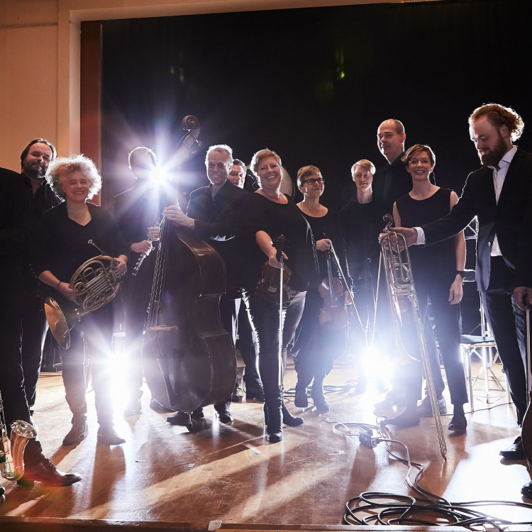 Ensamble med musiker står på rad framför kameran och lampor skapar motljuseffekt i bilden.