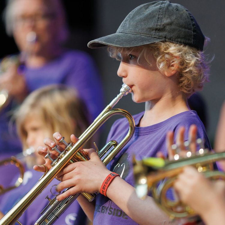 Liten pojke med keps spelar trumpet.