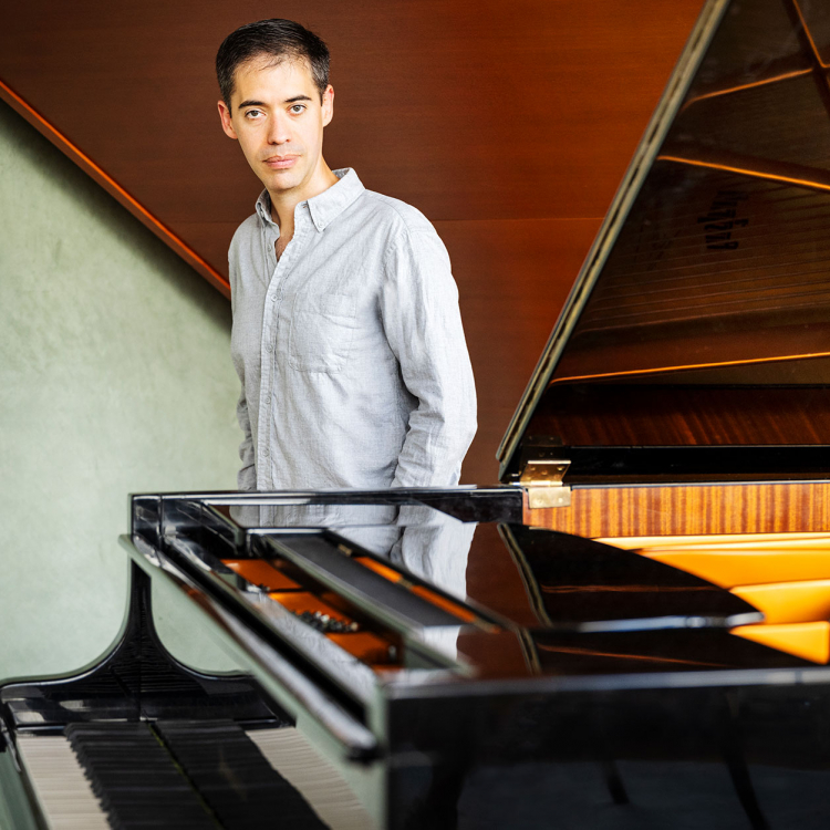 Juan Zurutuza står bakom en flygel och tittar in i kameran.