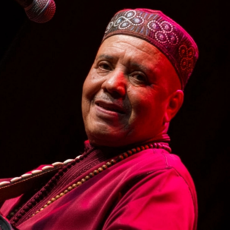 Man iklädd rösaröda kläder tittar in i kameran. Bilden är tagen i profil mot mörk bakgrund.