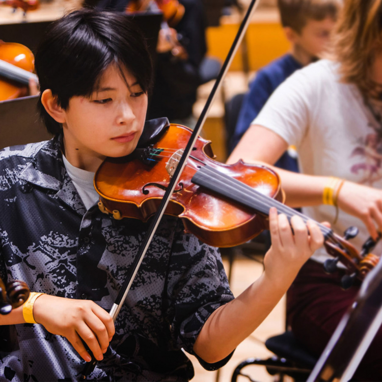 Ung violinist spelar på sitt instrument på scen, omgiven av andra unga musiker.
