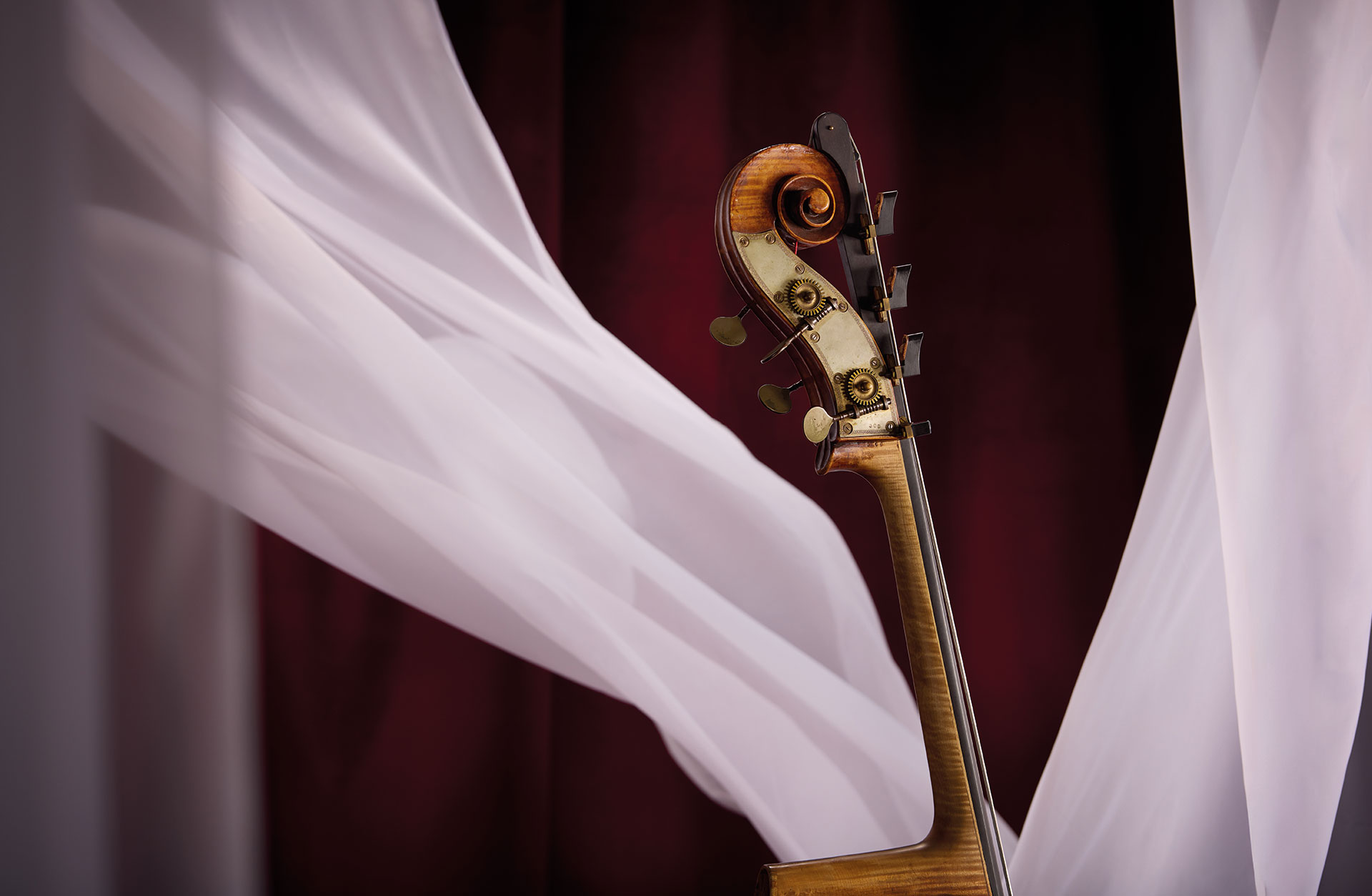 Toppen på en kontrabas fotad mot röd bakgrund med böljande vita tyger.