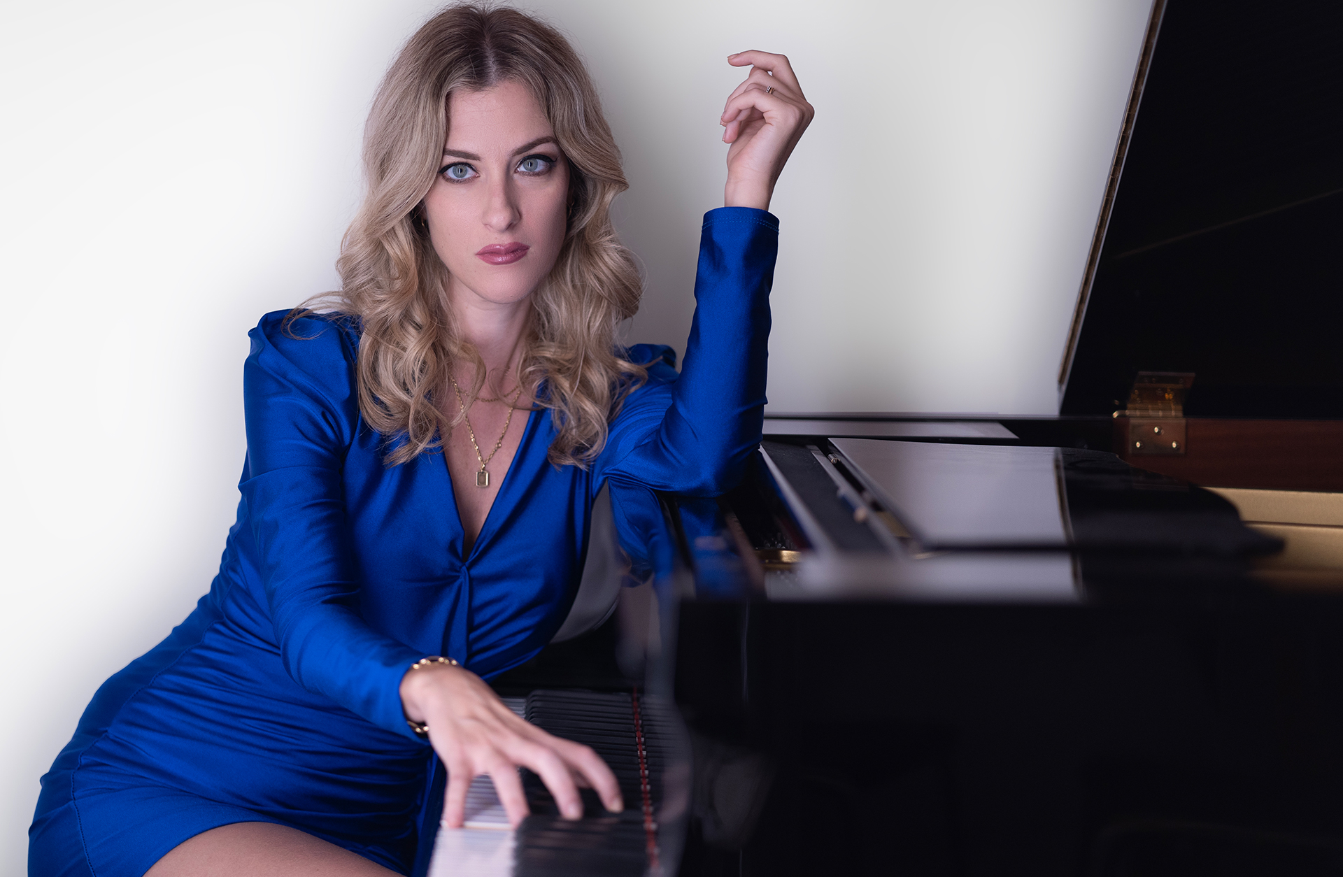 En ung blond kvinna sitter vid en flygel. Hon är finklädd och sminkad.