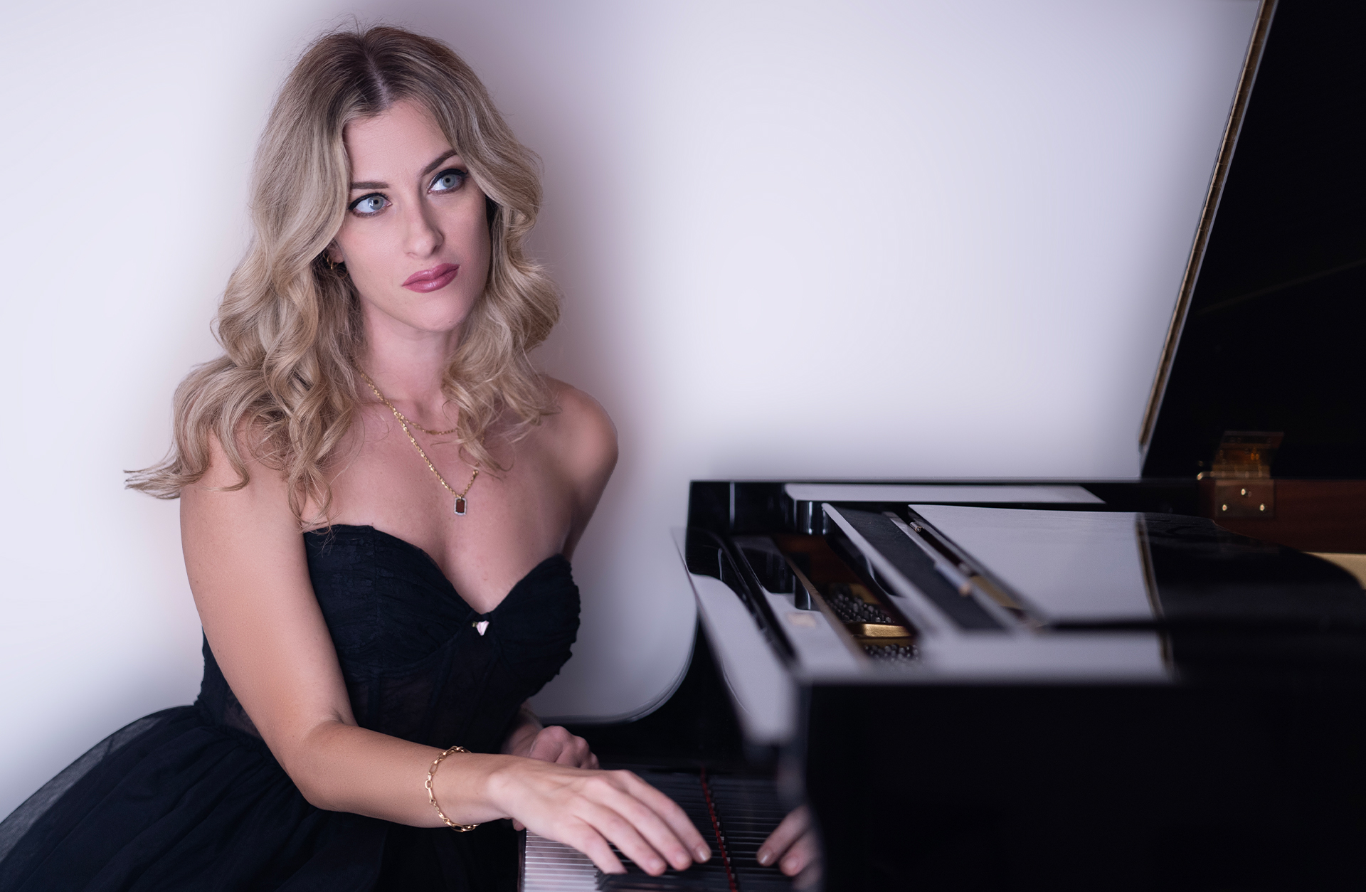 En ung blond kvinna sitter vid en flygel. Hon är finklädd och sminkad.
