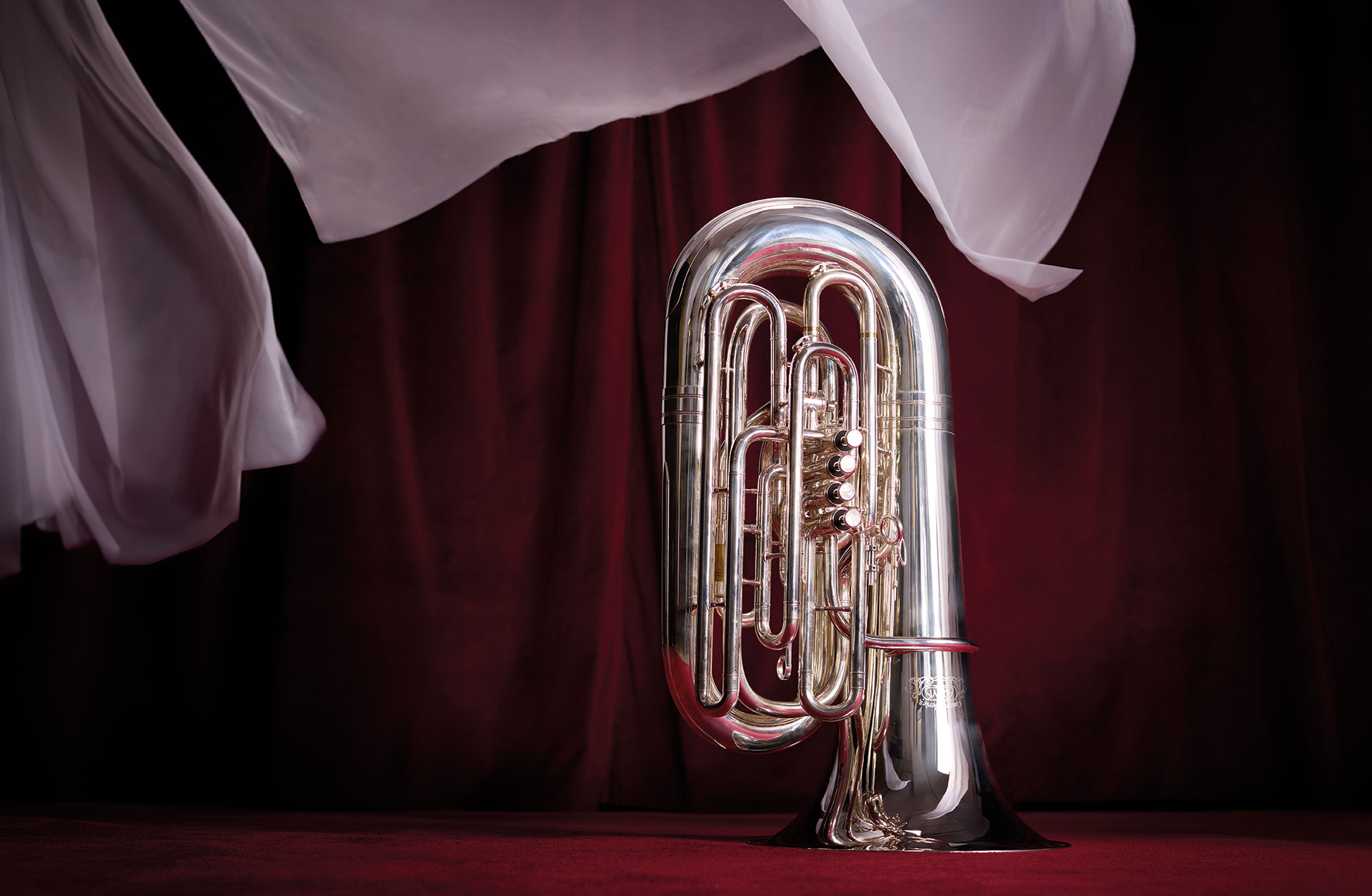 En tuba fotad mot röd bakgrund med böljande vita tyger.