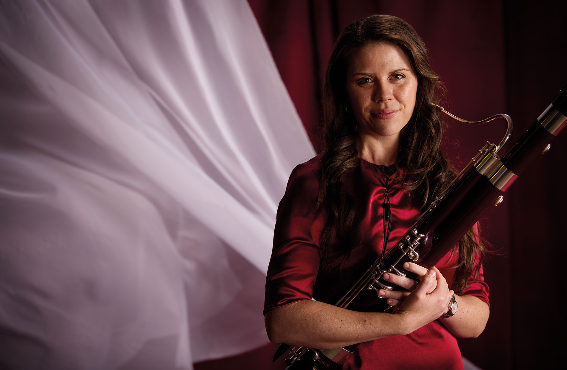 Fagottisten Kaitlyn Cameron med fagotten i famnen, fotad mot röd bakgrund med vita böljande tyger.