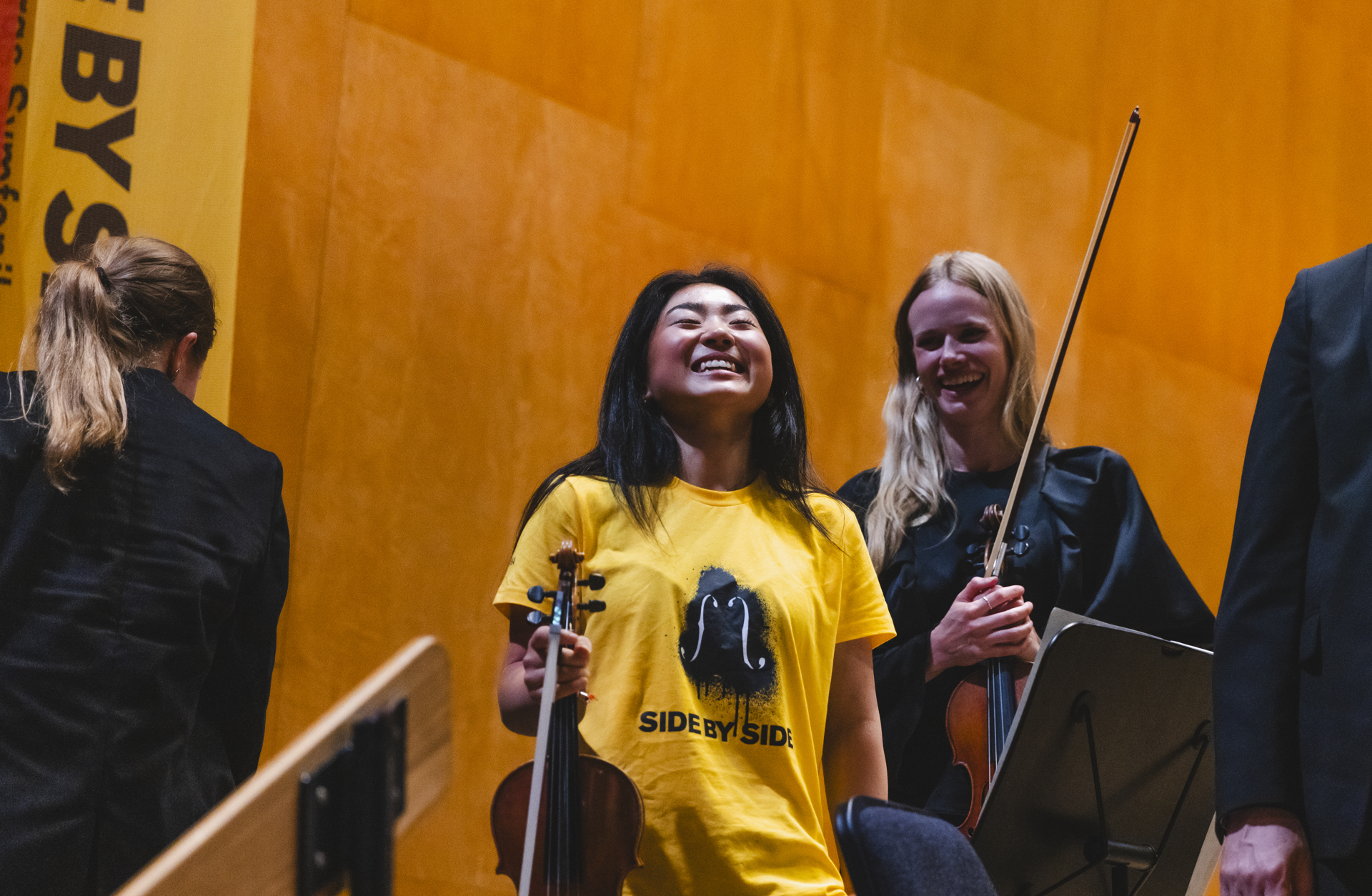 En glad mörkhårig tjej i gul t-shirt skrattar efter konserten.