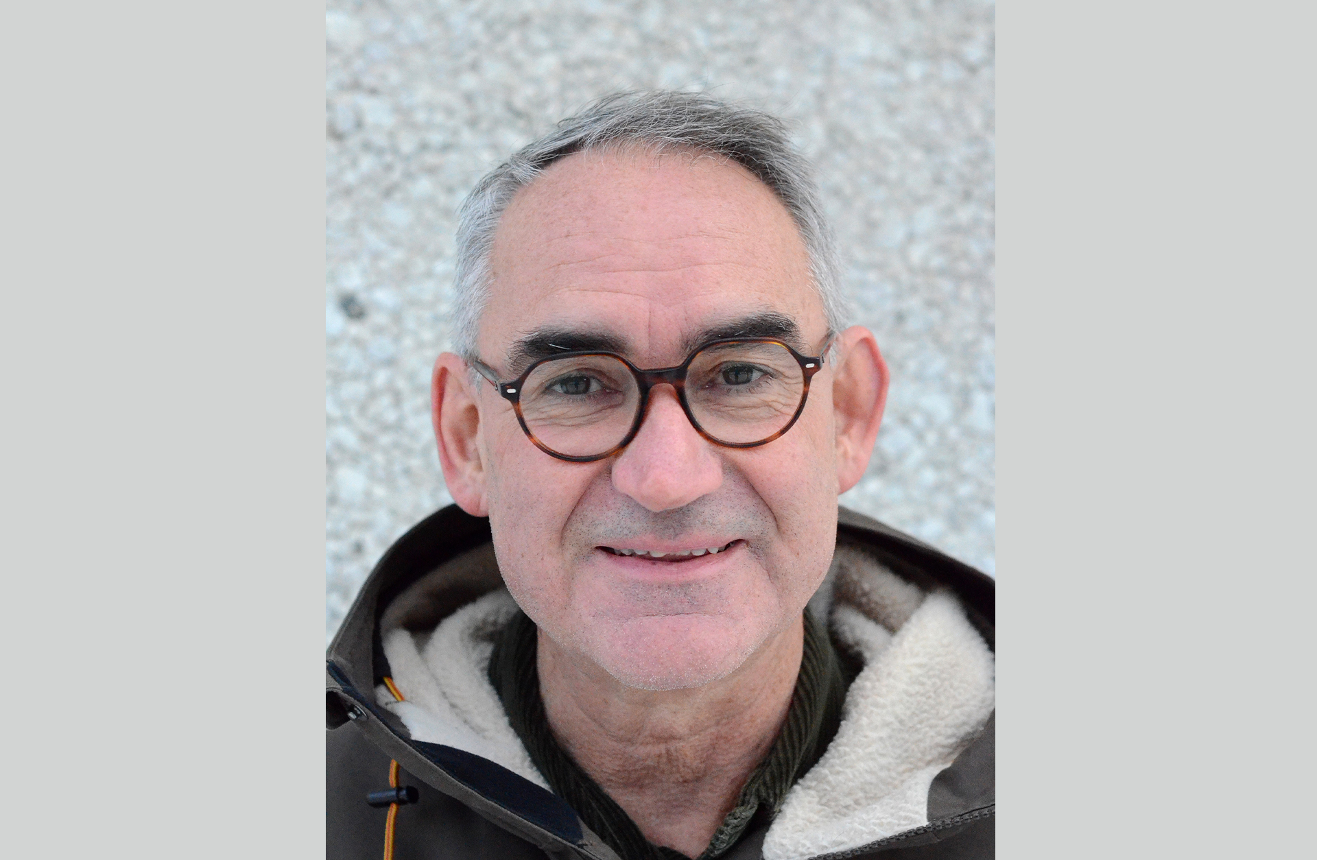 Ett ansiktsporträtt av en glad äldre man med glasögon och grått hår.