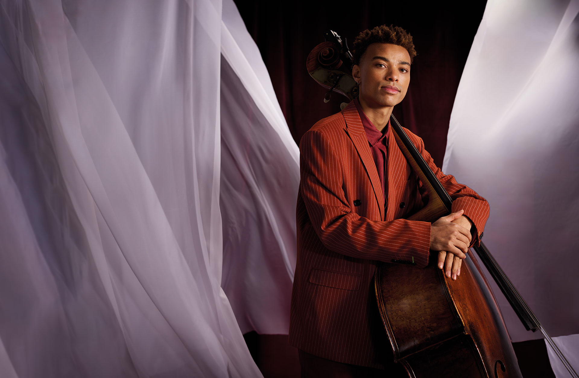 Kontrabasisten Taylor Abbitt med tuban i famnen, fotad mot röd bakgrund med vita böljande tyger.