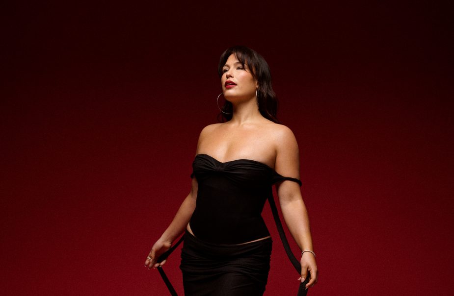 En kvinna står framför en vinröd vägg, Hon har en svart klänning på sig.