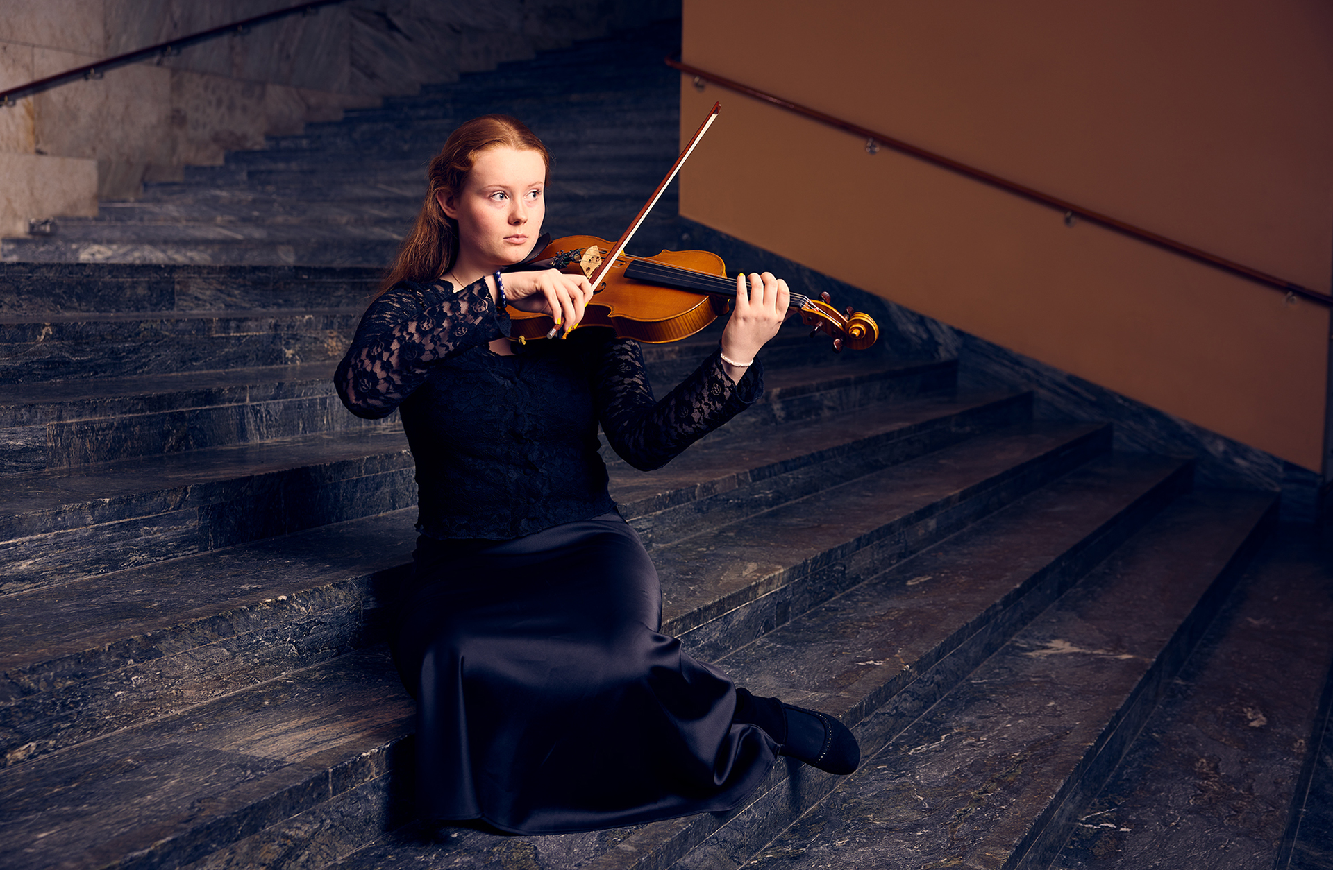 En ung kvinna sitter i en trappa och spelar viola