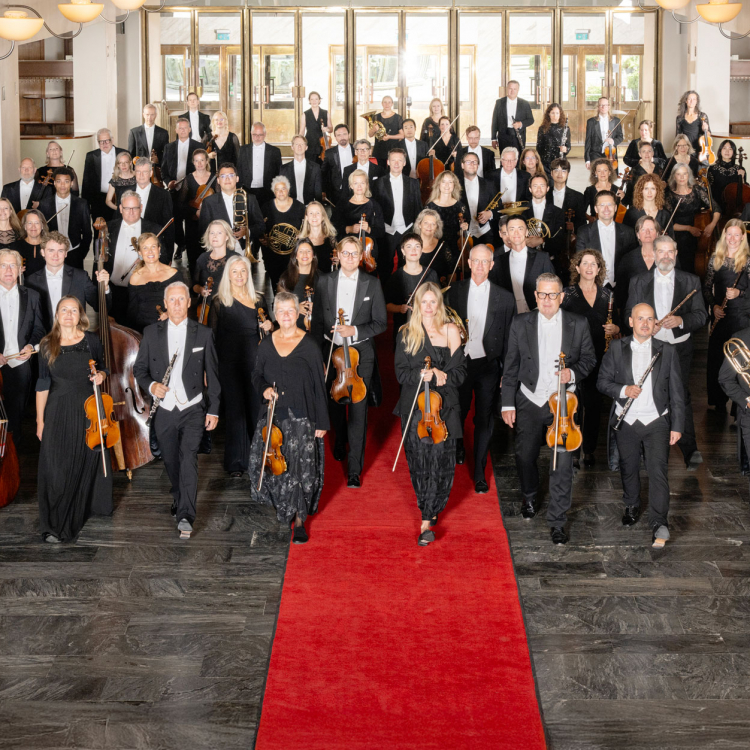 En konsertklädd symfoniorkester håller sina instrument och står i garderobshallen i Göteborgs Konserthus.