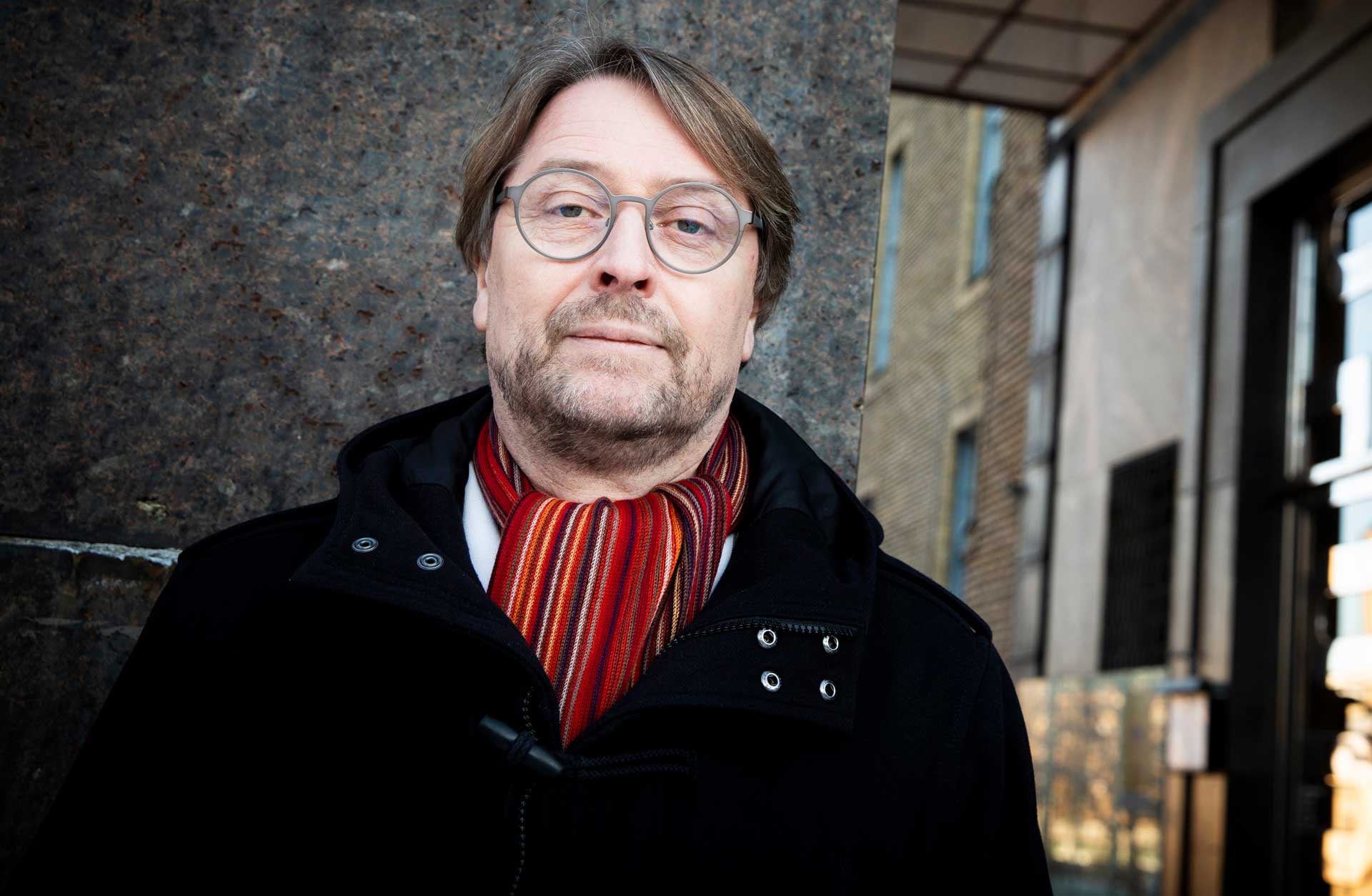 Porträtt av en korthårig man i glasögon. Han står utomhus iklädd en vinterjacka och en randig halsduk.
