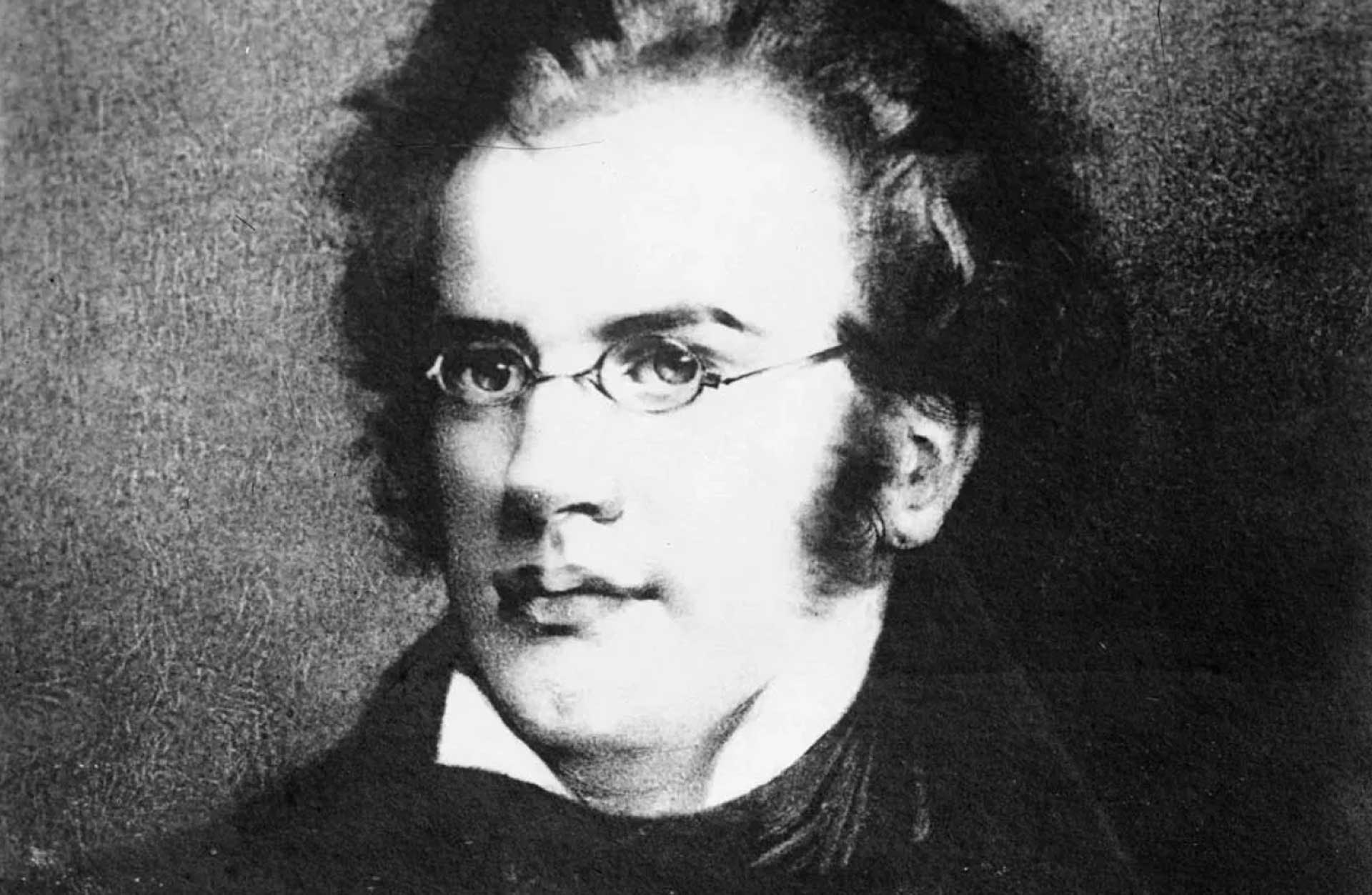 Svartvitt porträtt av Franz Schubert. En man med kort ostyrigt hår och glasögon.